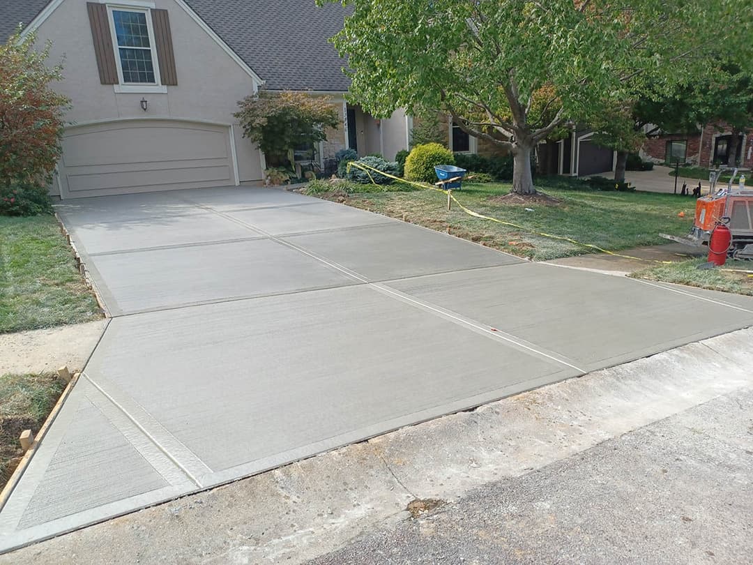 Newly poured concrete driveway in residential setting with green landscaping.