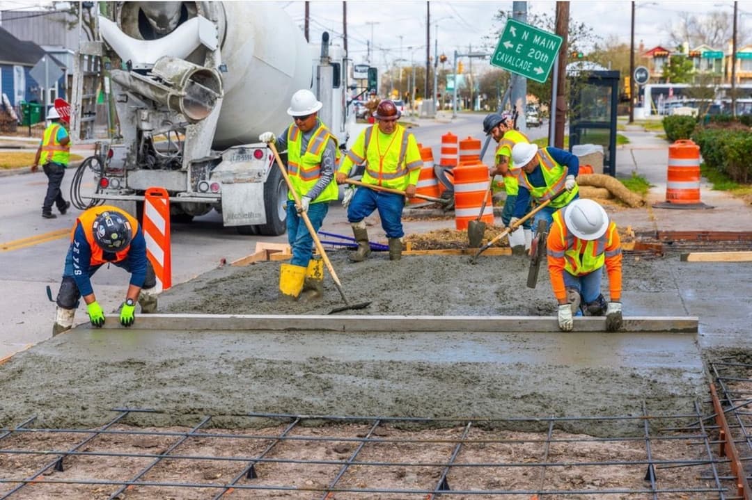 Construction workers pouring and leveling concrete for pavement repair on a city street.