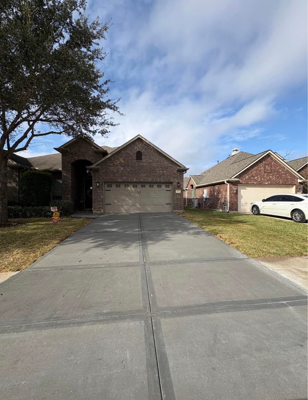 Brick house with a garage, driveway, and landscaped front yard under a blue sky.