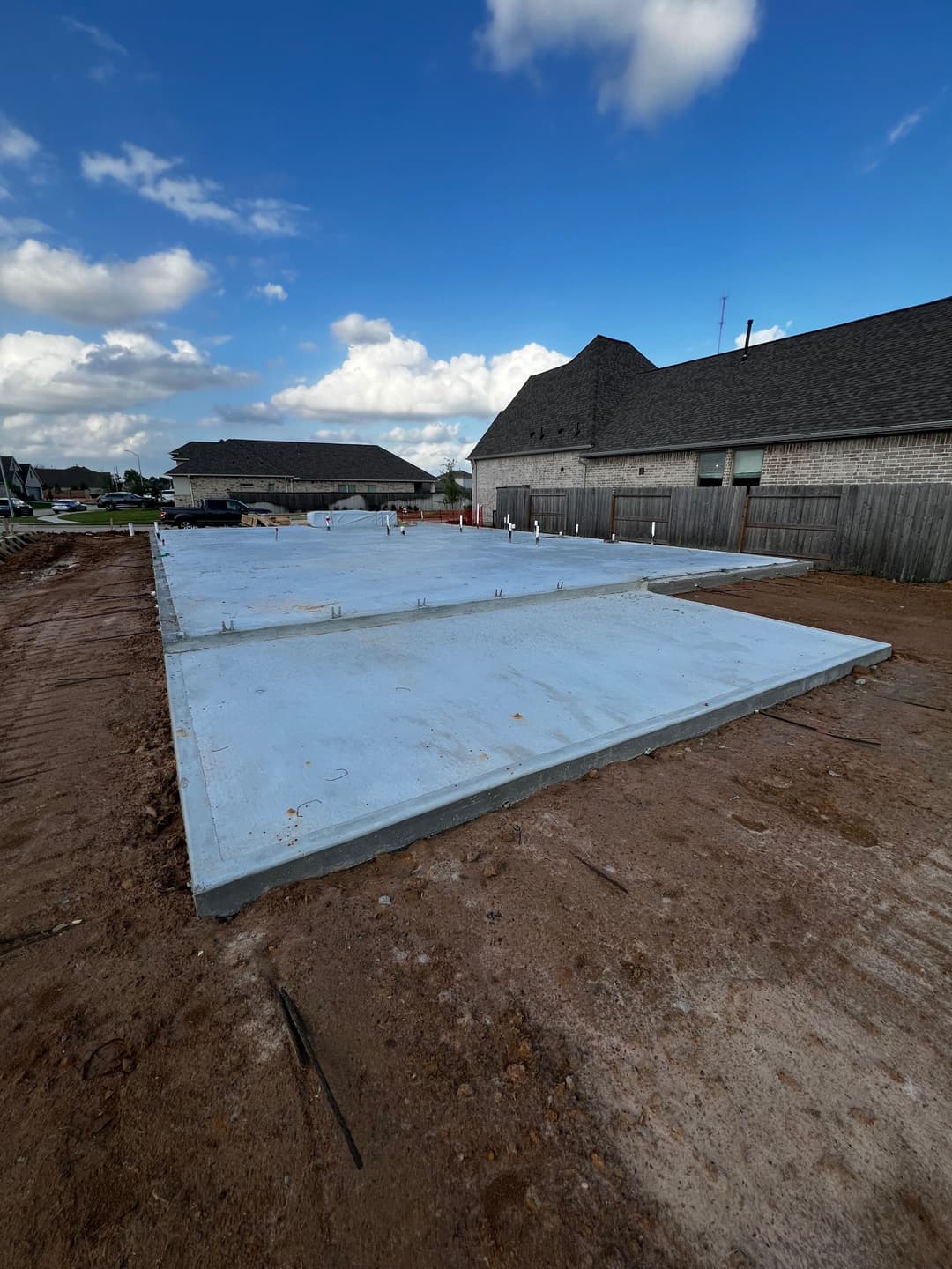 New concrete foundation slab on a construction site under a cloudy blue sky.