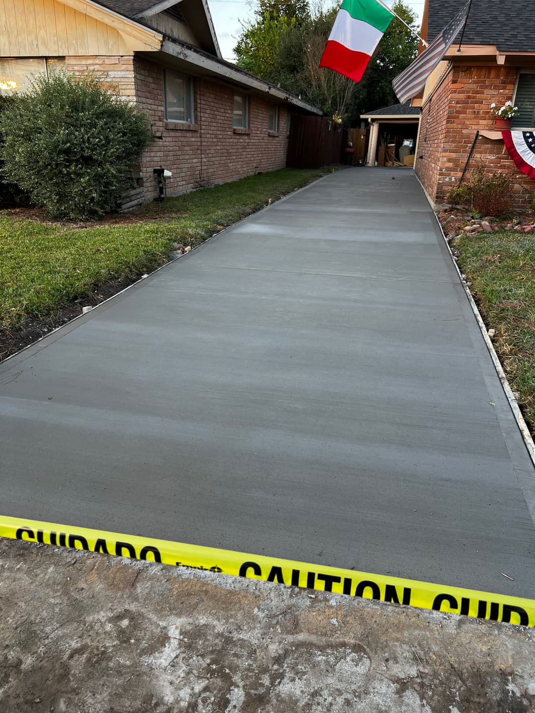 Freshly poured concrete driveway with caution tape and Italian flag in the background.