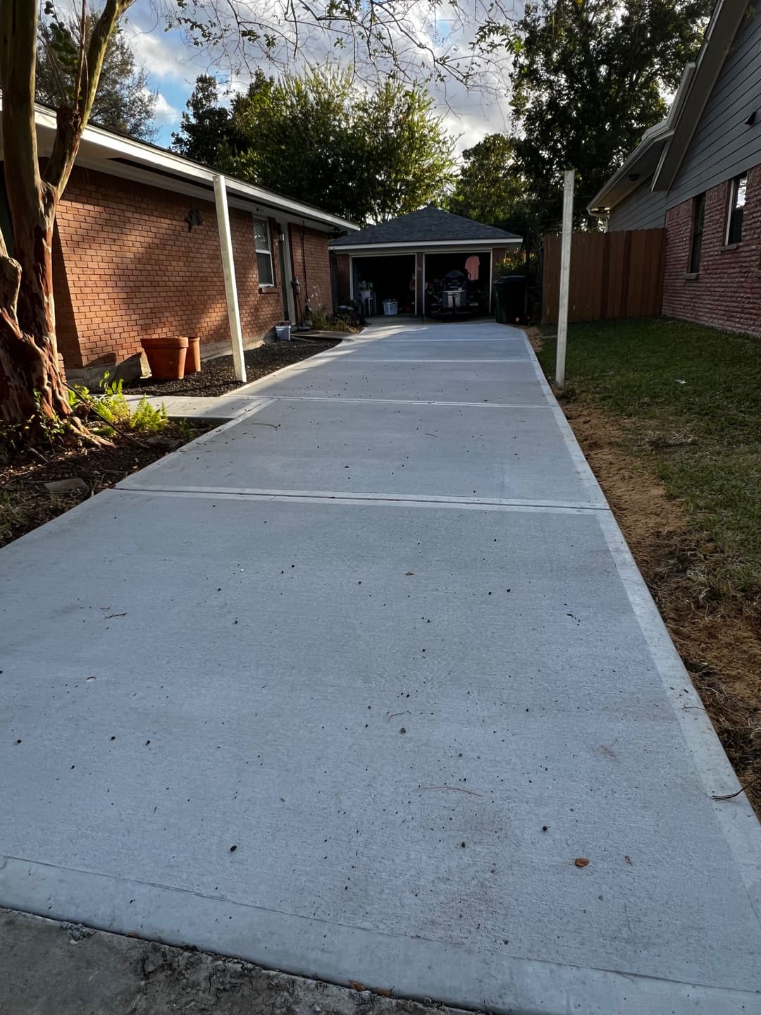 Newly poured concrete driveway leading to a carport, surrounded by greenery and brick homes.