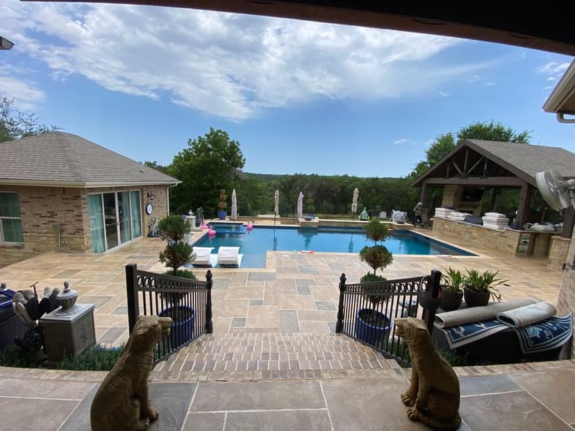Luxury backyard with pool, stone patio, outdoor kitchen, and scenic views.